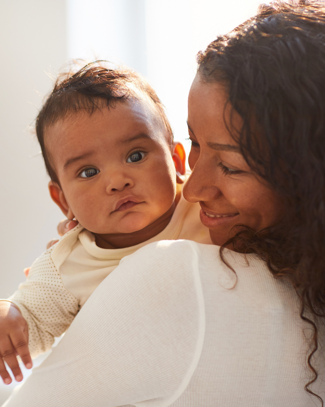 Woman holding a baby, both softly lit and looking at each other