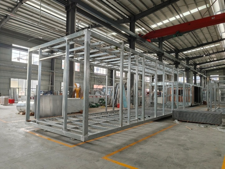 Metal frame structure of a building under construction inside a factory with a red crane.