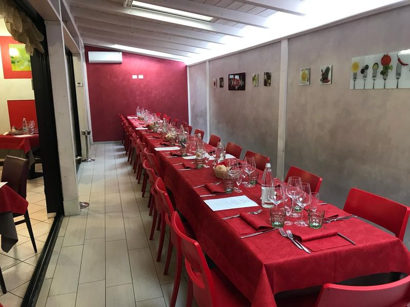 Lungo tavolo rosso apparecchiato per un pasto in un ristorante con pareti rosse e bianche e sedie rosse.