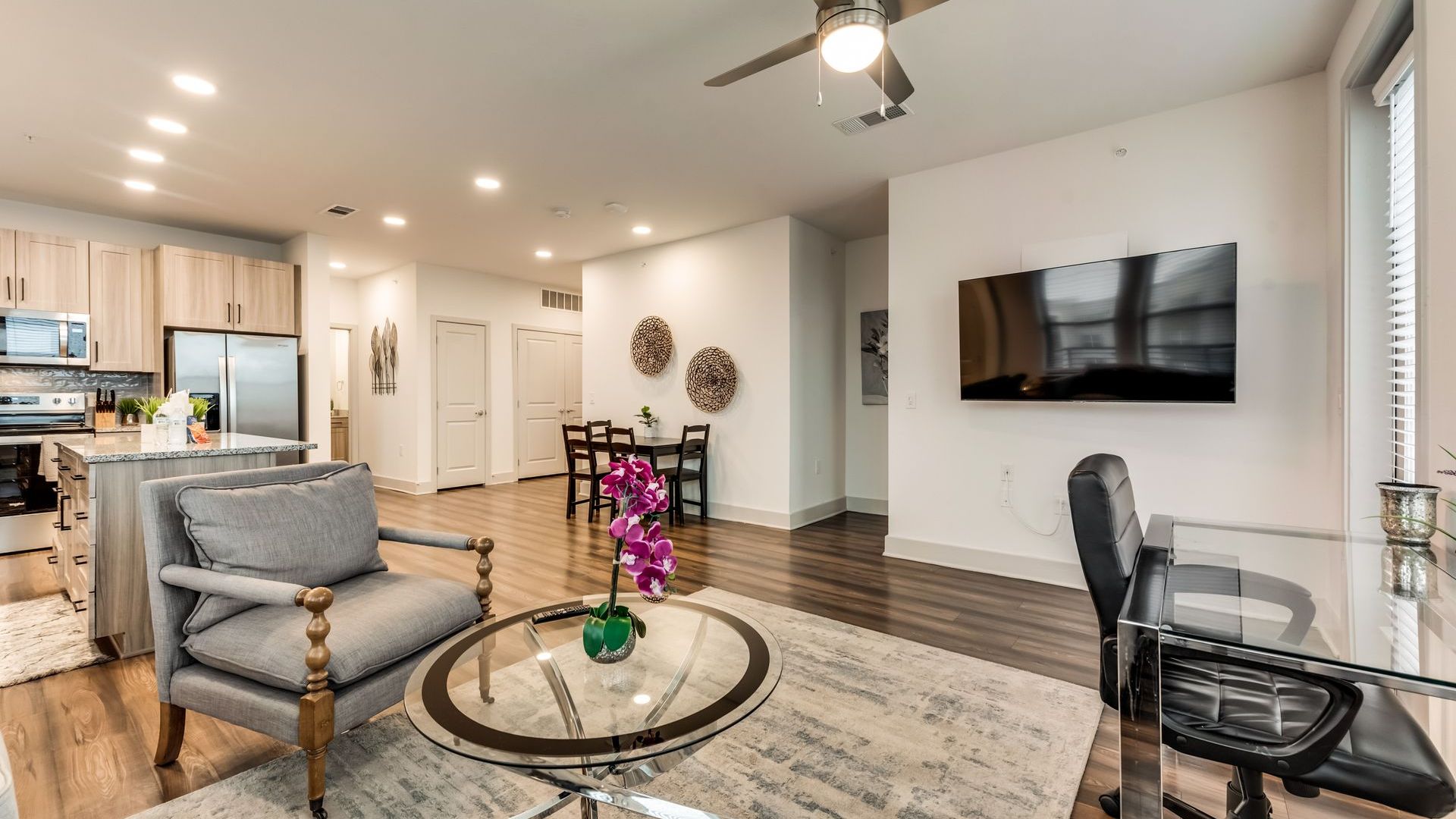 A living room with a ceiling fan and a flat screen tv on the wall.
