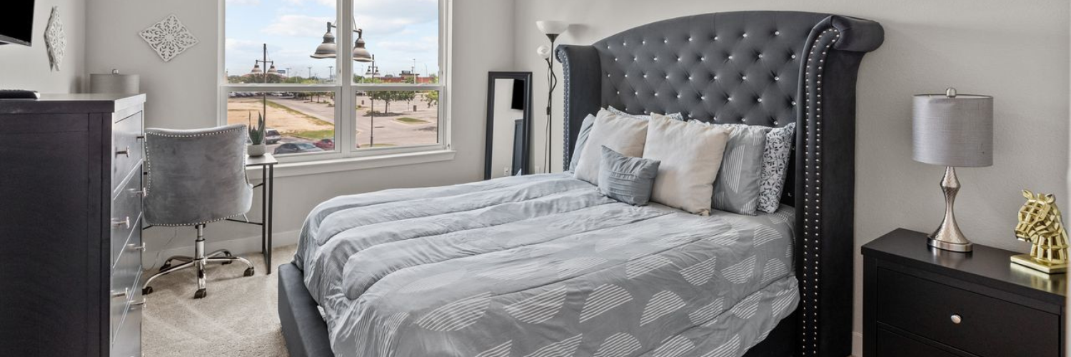 A bedroom with a bed , nightstand , desk and window.