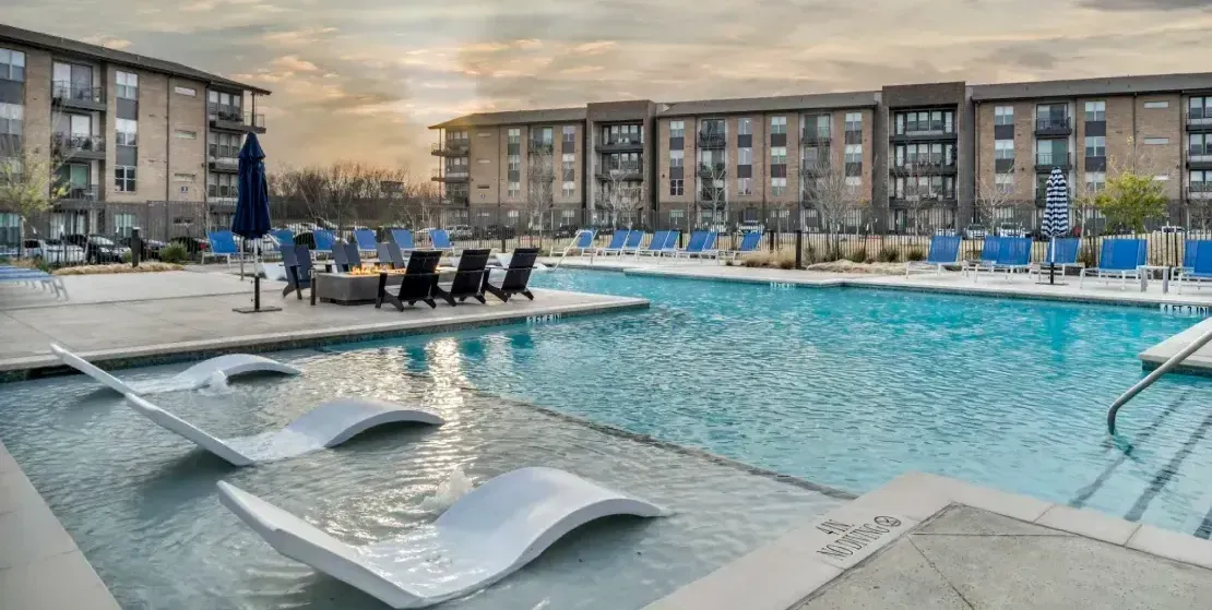 A large swimming pool surrounded by chairs and umbrellas in front of a building.
