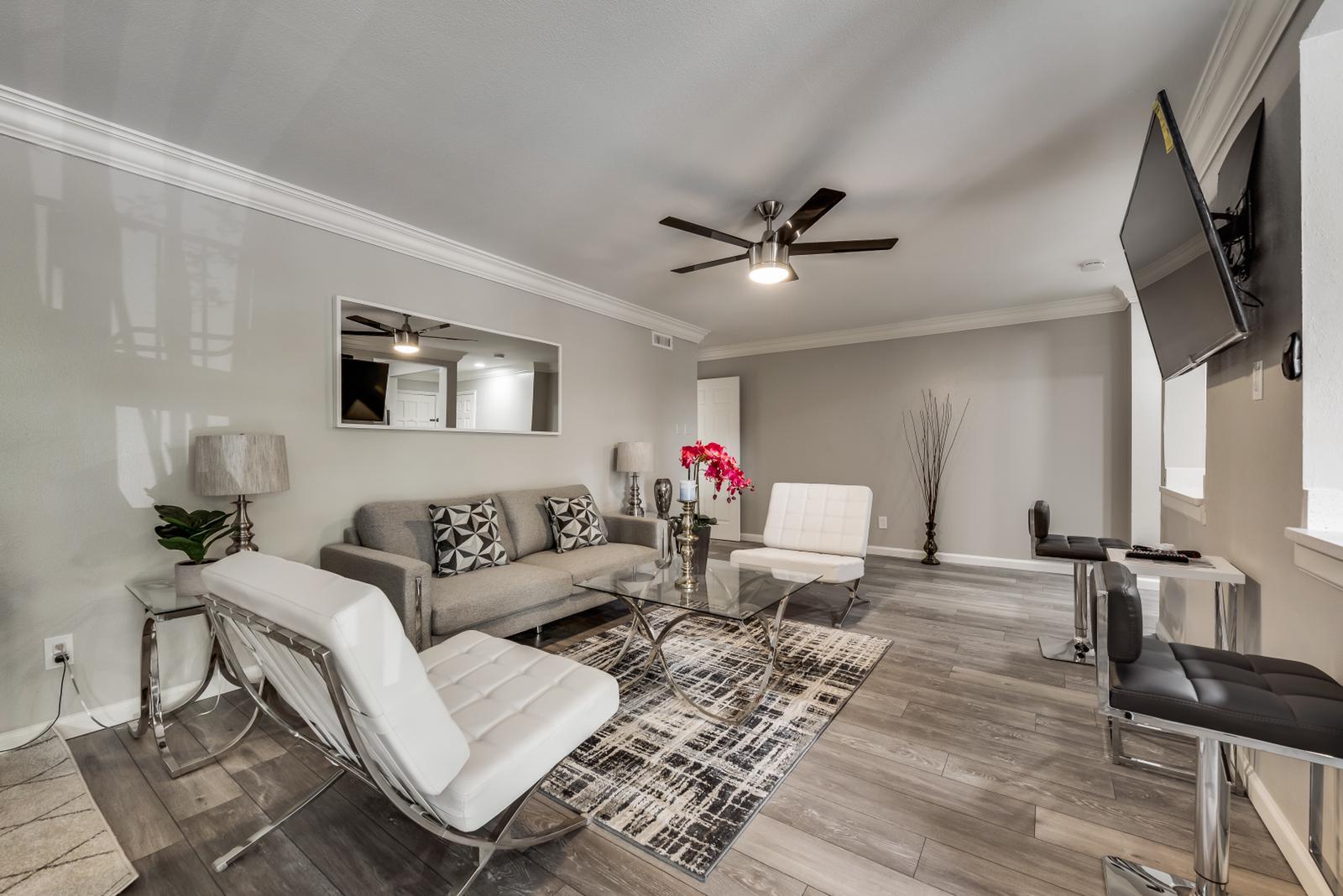 A living room with a couch , chairs , a television and a ceiling fan.