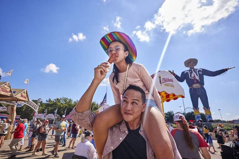 A man is carrying a girl on his shoulders at a carnival.