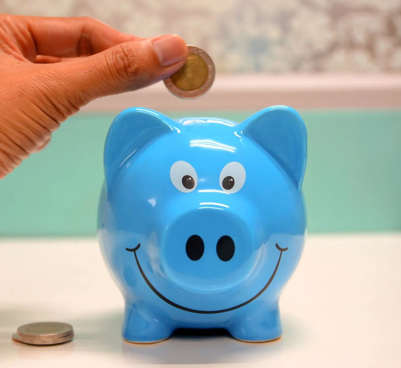 A person is putting a coin into a blue piggy bank