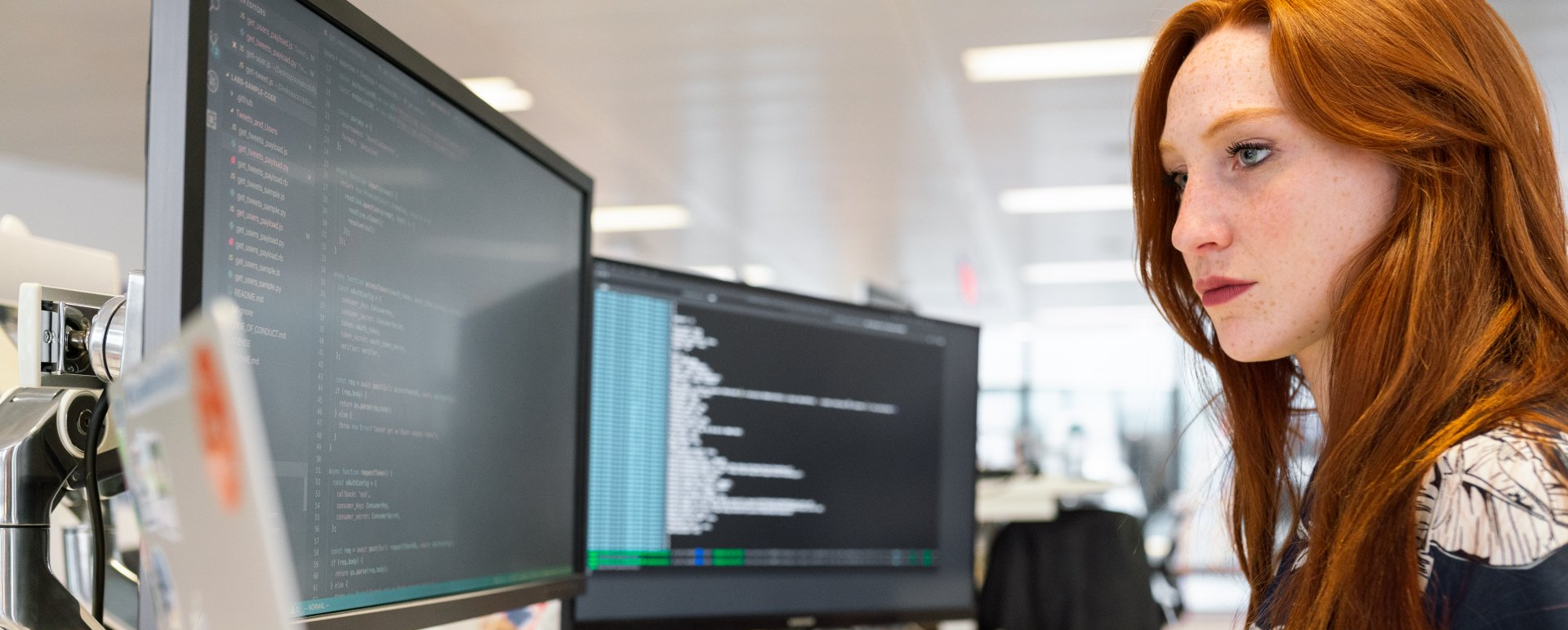 A woman with red hair is looking at a computer screen.