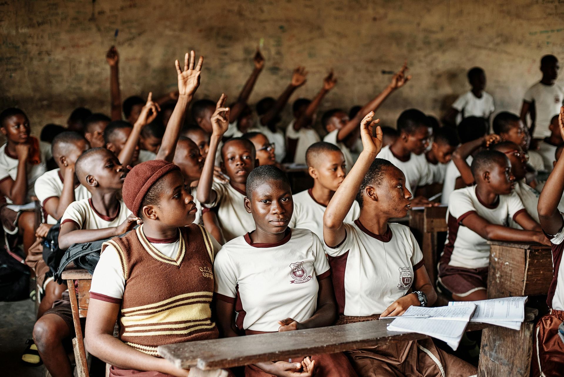 A group of children are raising their hands in a classroom.