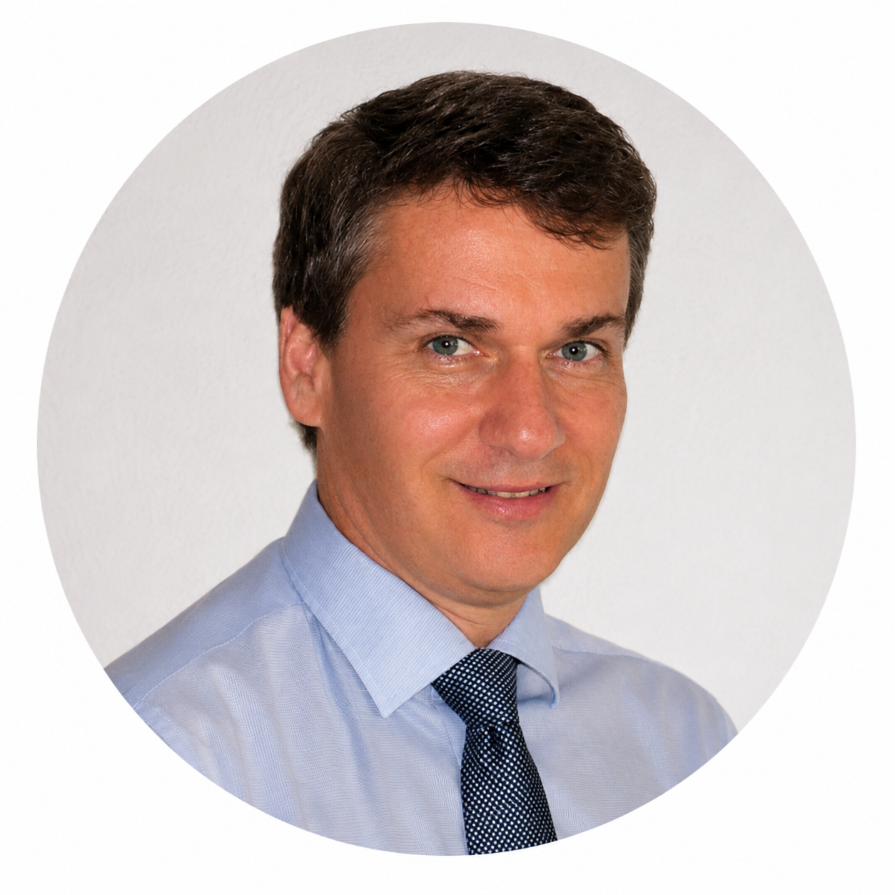 Portrait d'un homme souriant, portant une chemise bleu clair et une cravate, sur fond blanc.