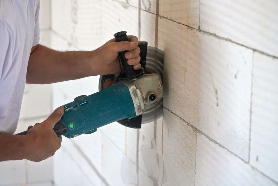 Person using a green angle grinder to cut a white tiled wall