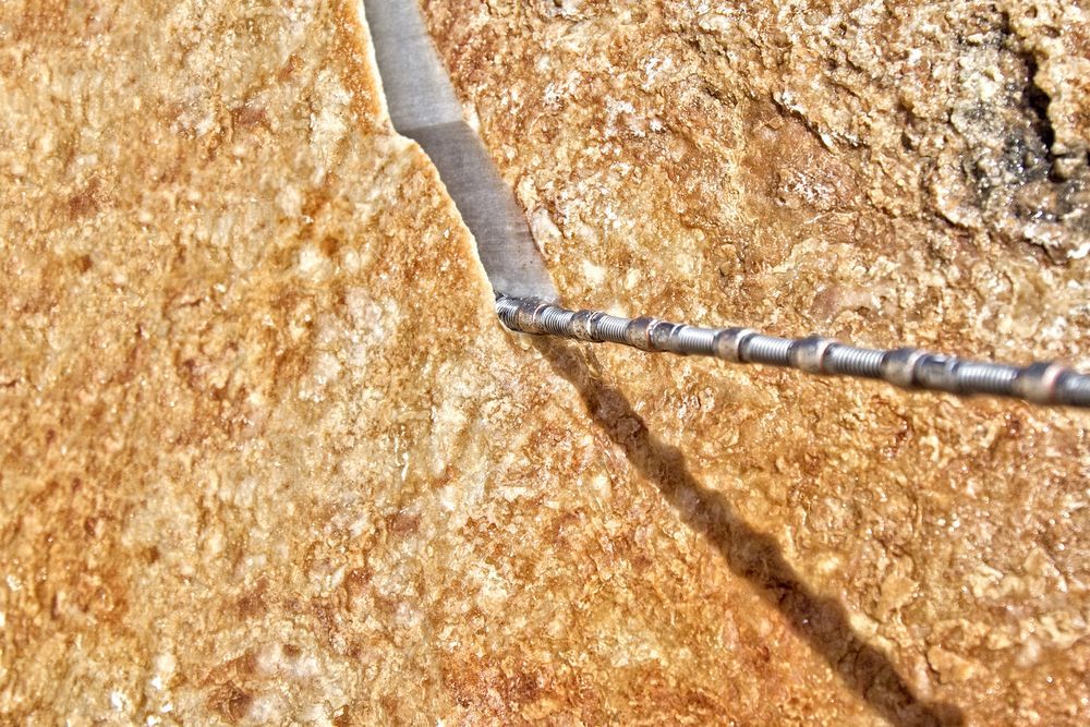 Close-up of a cracked tan rock surface with a thin metal rod crossing diagonally