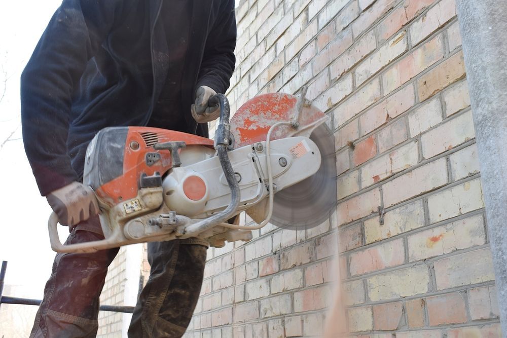 Worker using a concrete cut-off saw to cut into a brick wall outdoors