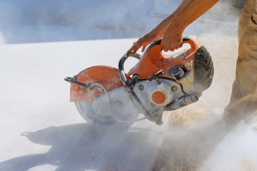 Person operating a handheld power saw cutting concrete, with dust and debris flying.