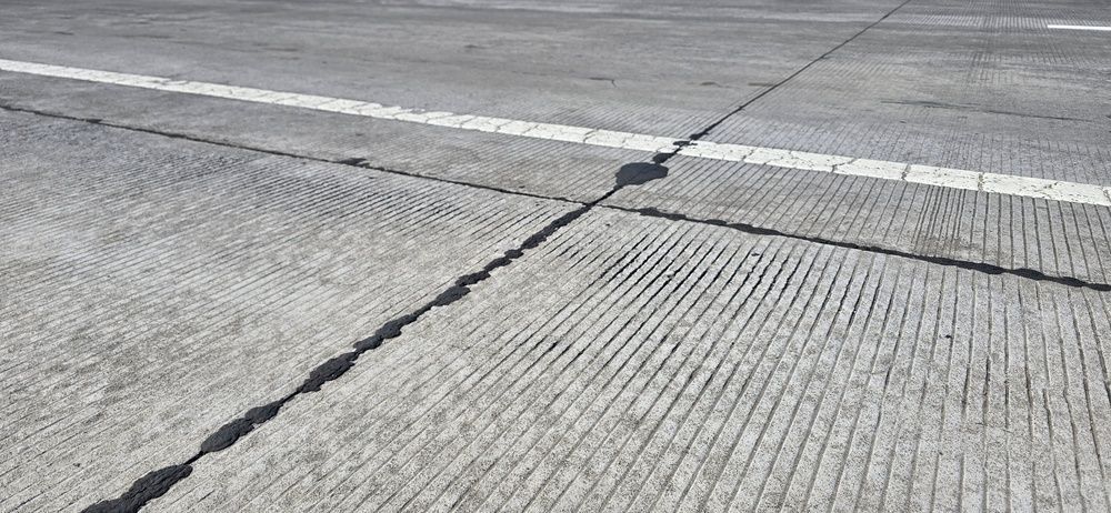 Cracked concrete road surface with a rough seam across the lane