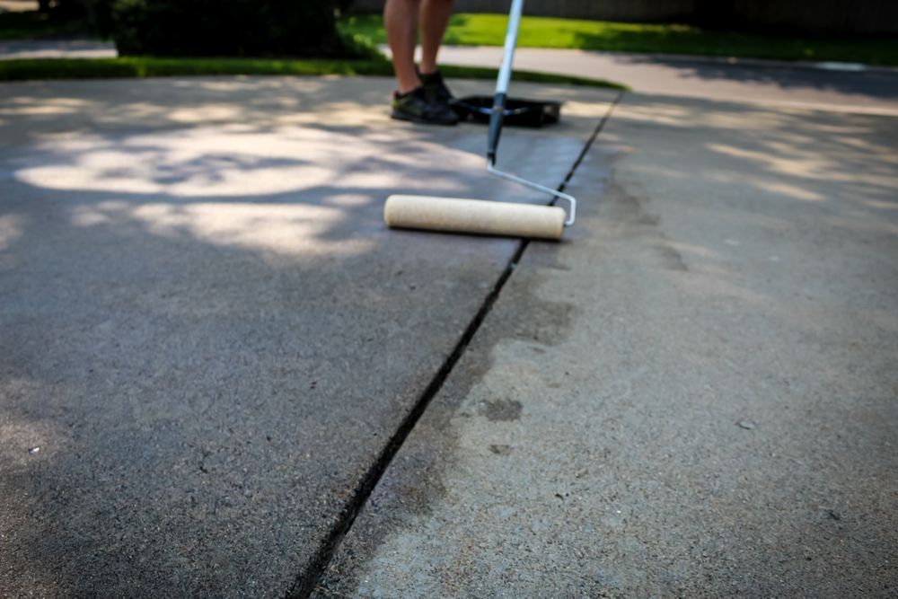 Person rolling gray coating onto a concrete driveway crack outdoors