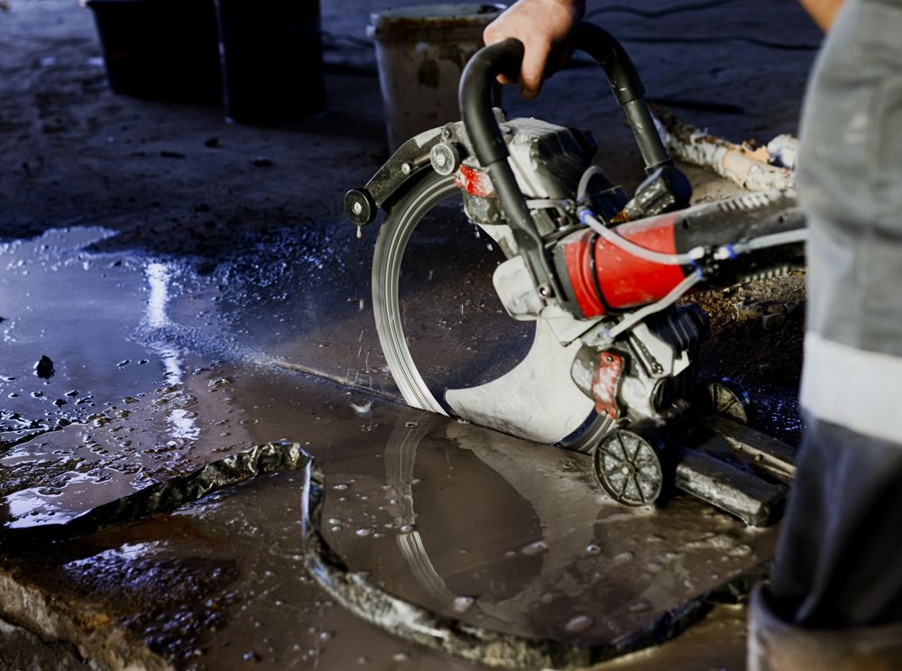Worker using a concrete saw to cut pavement beside a wet street manhole