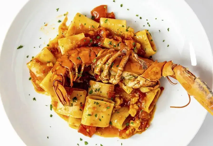 Piatto di pasta con aragosta in salsa di pomodoro, guarnito con prezzemolo.