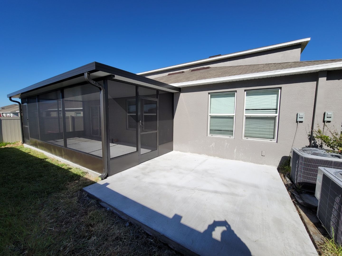 Screened porch attached to a house with concrete patio, blue sky, and green grass.