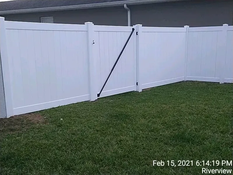 White vinyl fence with a gate in a grassy yard.