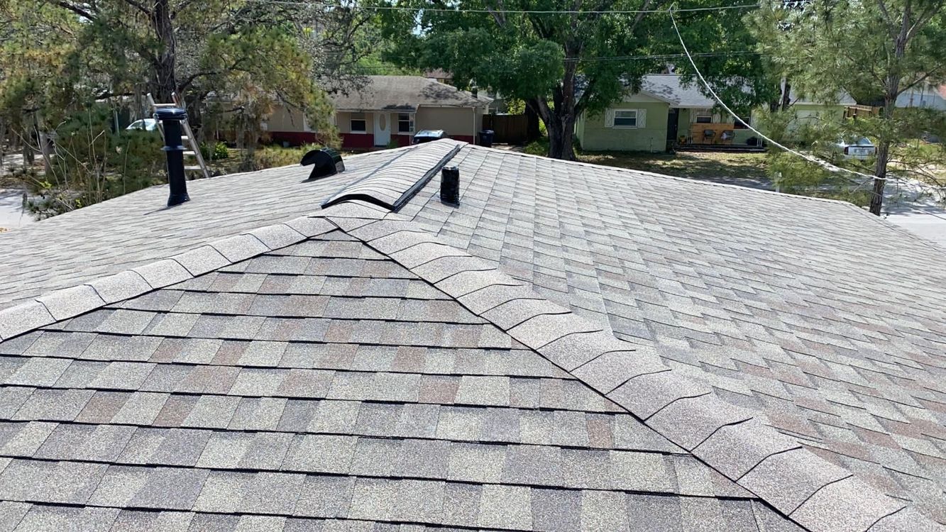 View of a gray shingle roof on a house, with chimneys and a clear sky in the background.