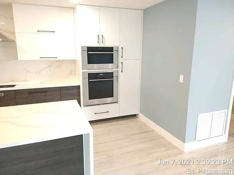 Modern kitchen with white and dark cabinets, stainless steel appliances, and a light blue wall.
