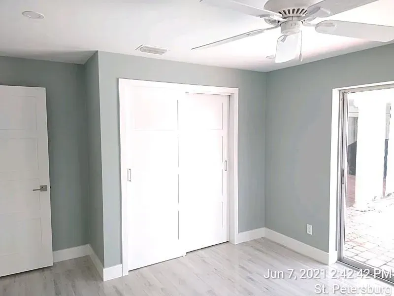 Empty bedroom with light blue walls, white doors and trim, ceiling fan, and sliding glass door.