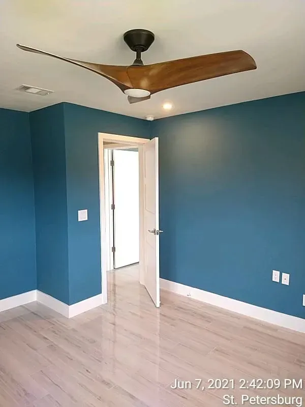 Blue-walled room with a wooden ceiling fan, open doorway, and light wood flooring.