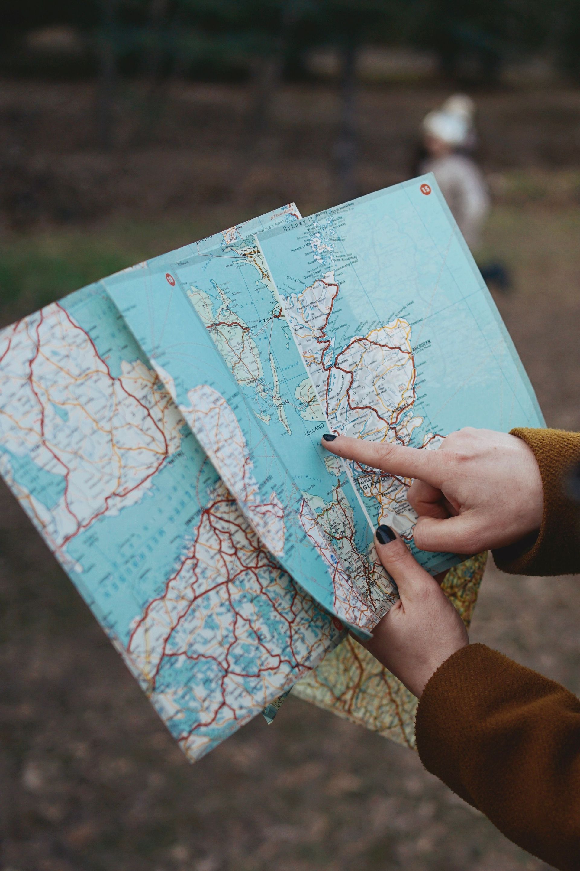 Hands pointing at a folded paper map outdoors, with a turquoise map centered in view.