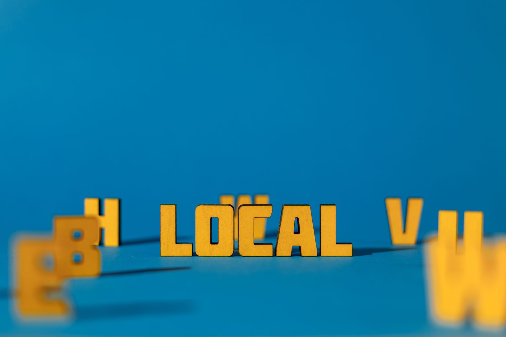 Bold yellow 3D “LOCAL V” text on a blue background, with blurred orange letters at the edges