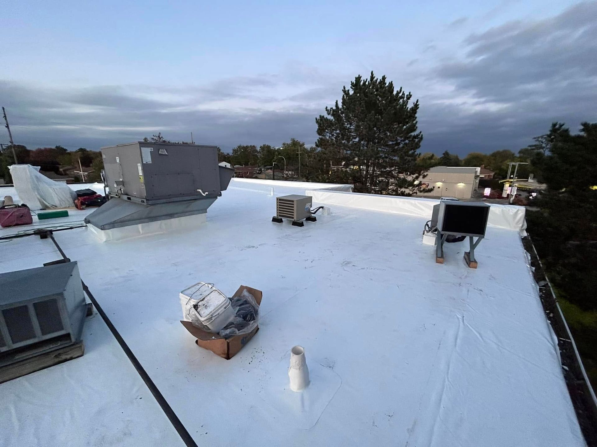 Flat white rooftop with HVAC units, vents, and a cloudy sky at dusk