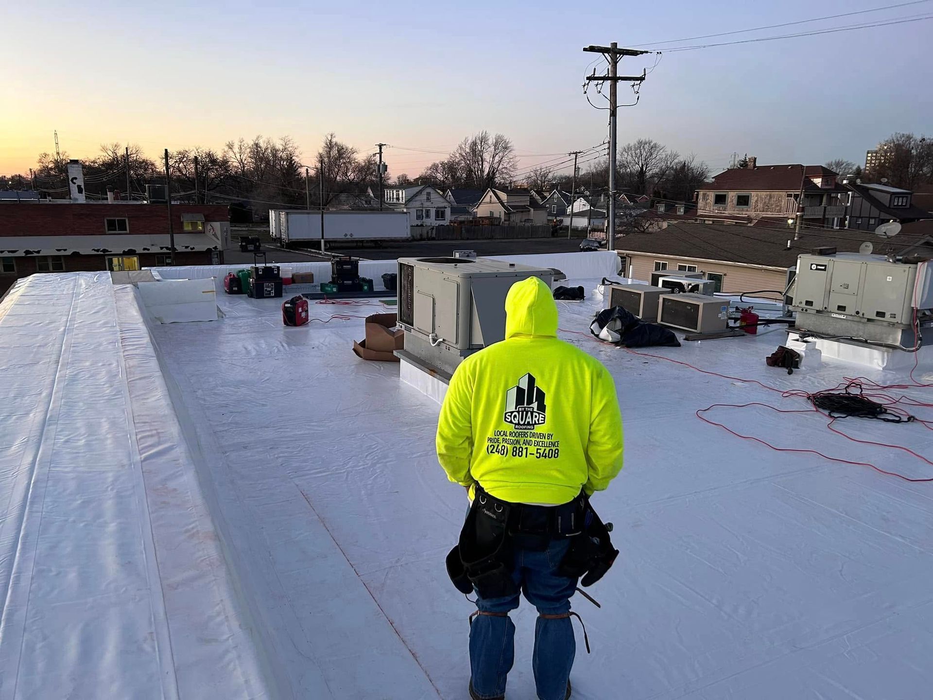 Worker in bright yellow jacket standing on a snowy rooftop at dawn.