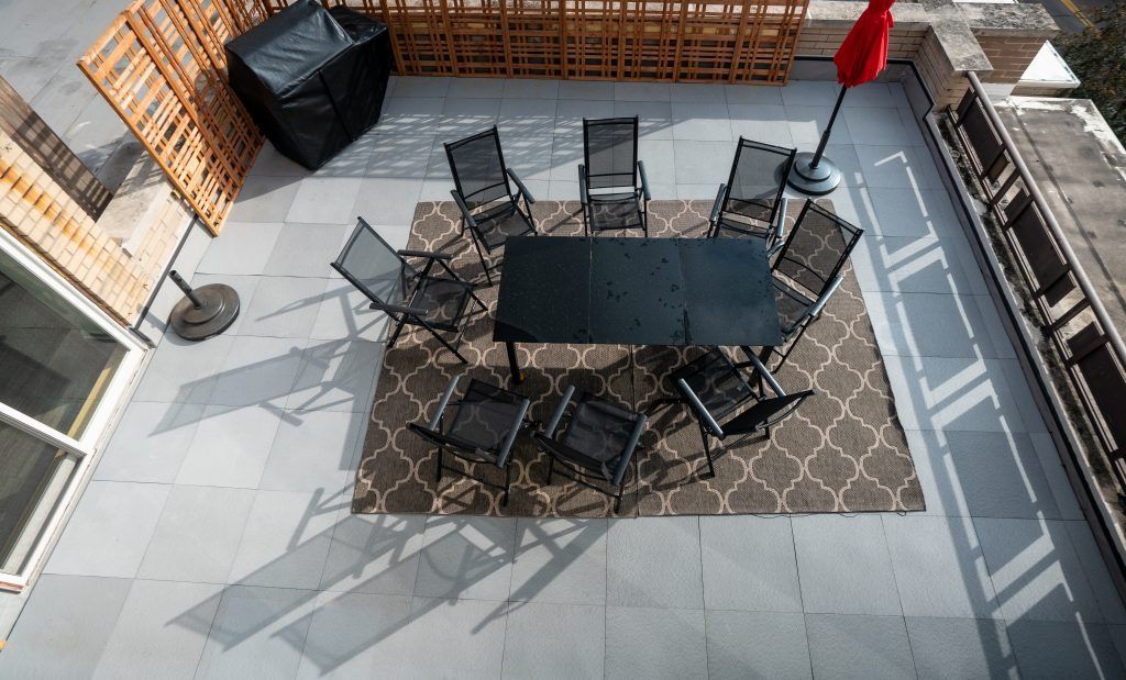 Rooftop patio with a long table, eight chairs, and a covered grill on a tiled terrace.