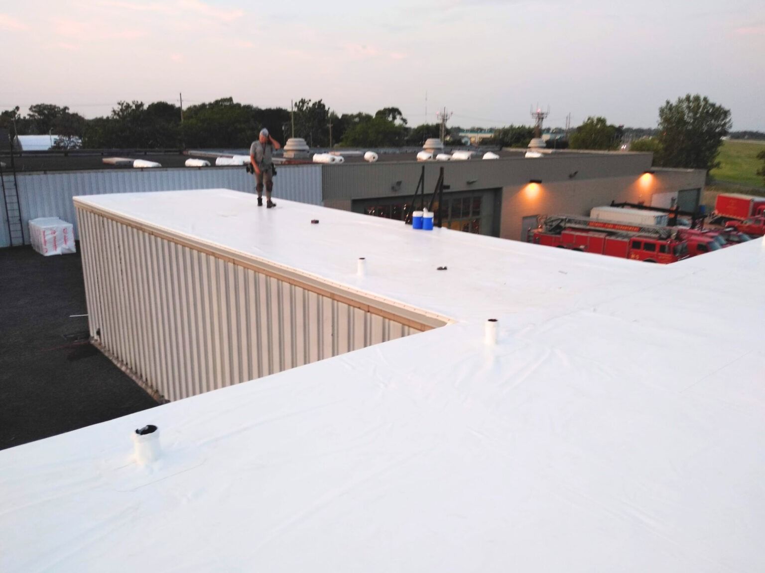 Rooftop with white membrane roof, a person standing near the edge, and construction equipment in the background