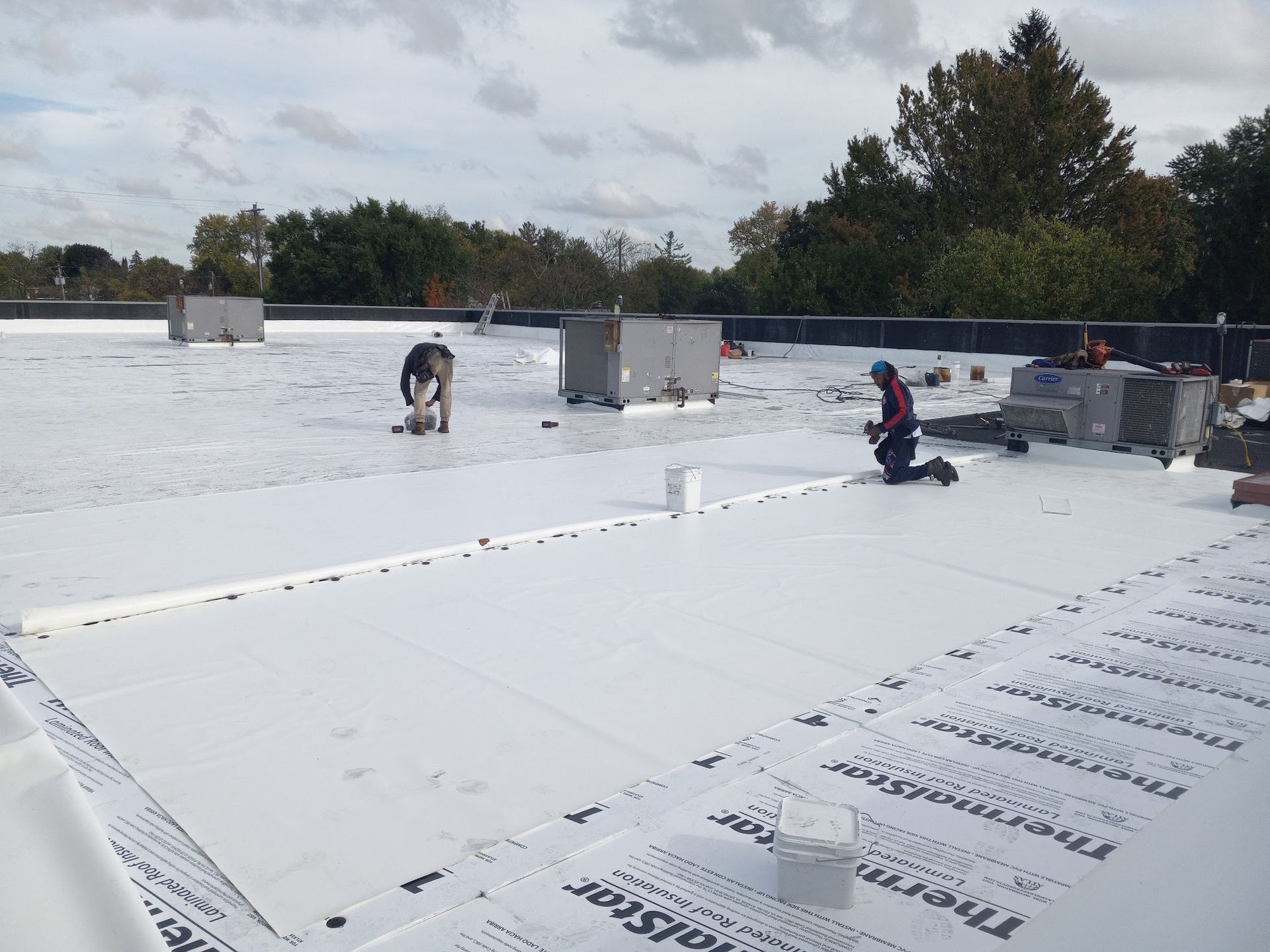 Workers installing rooftop insulation on a flat white roof under cloudy skies