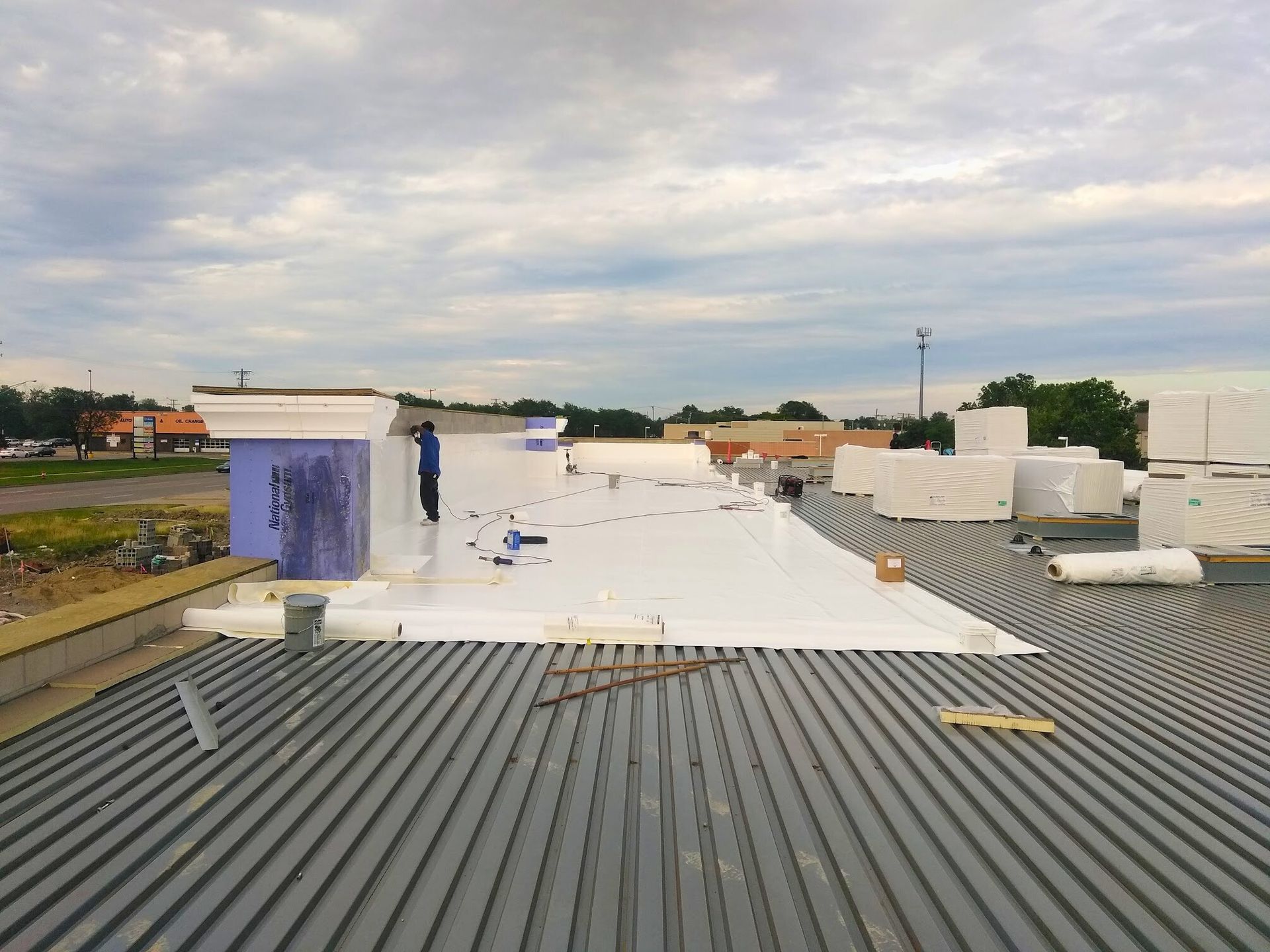 Rooftop with white waterproofing and gray corrugated surface under a cloudy sky.