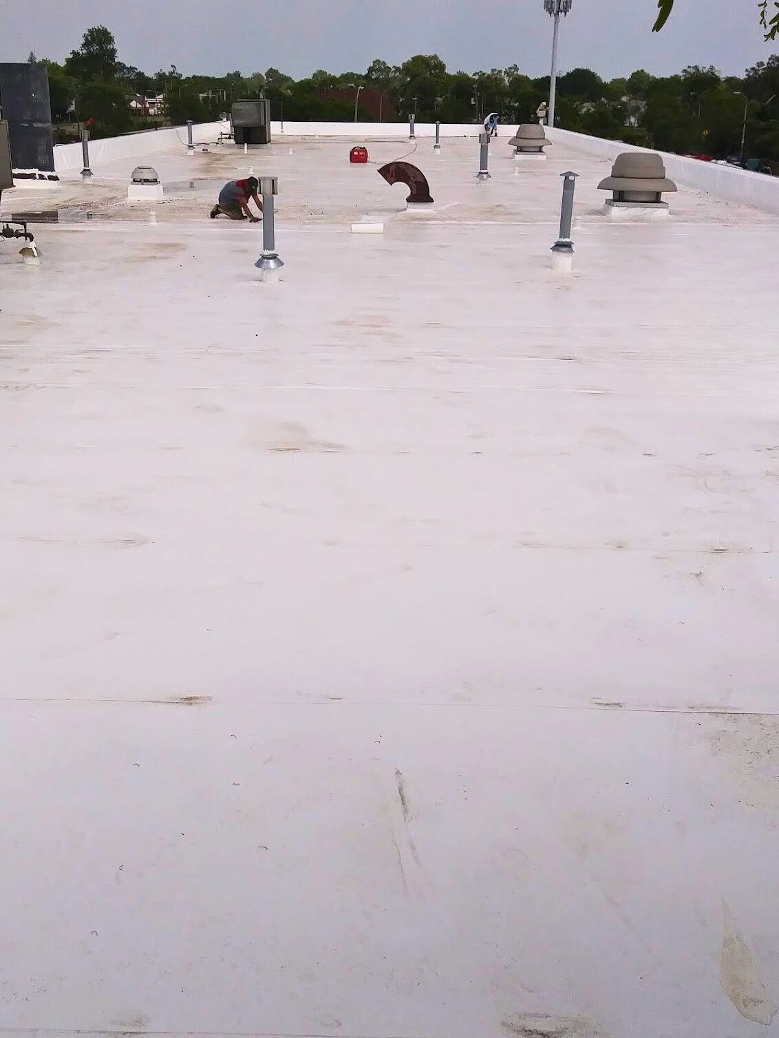 Flat white rooftop with a few vents and equipment under a cloudy sky