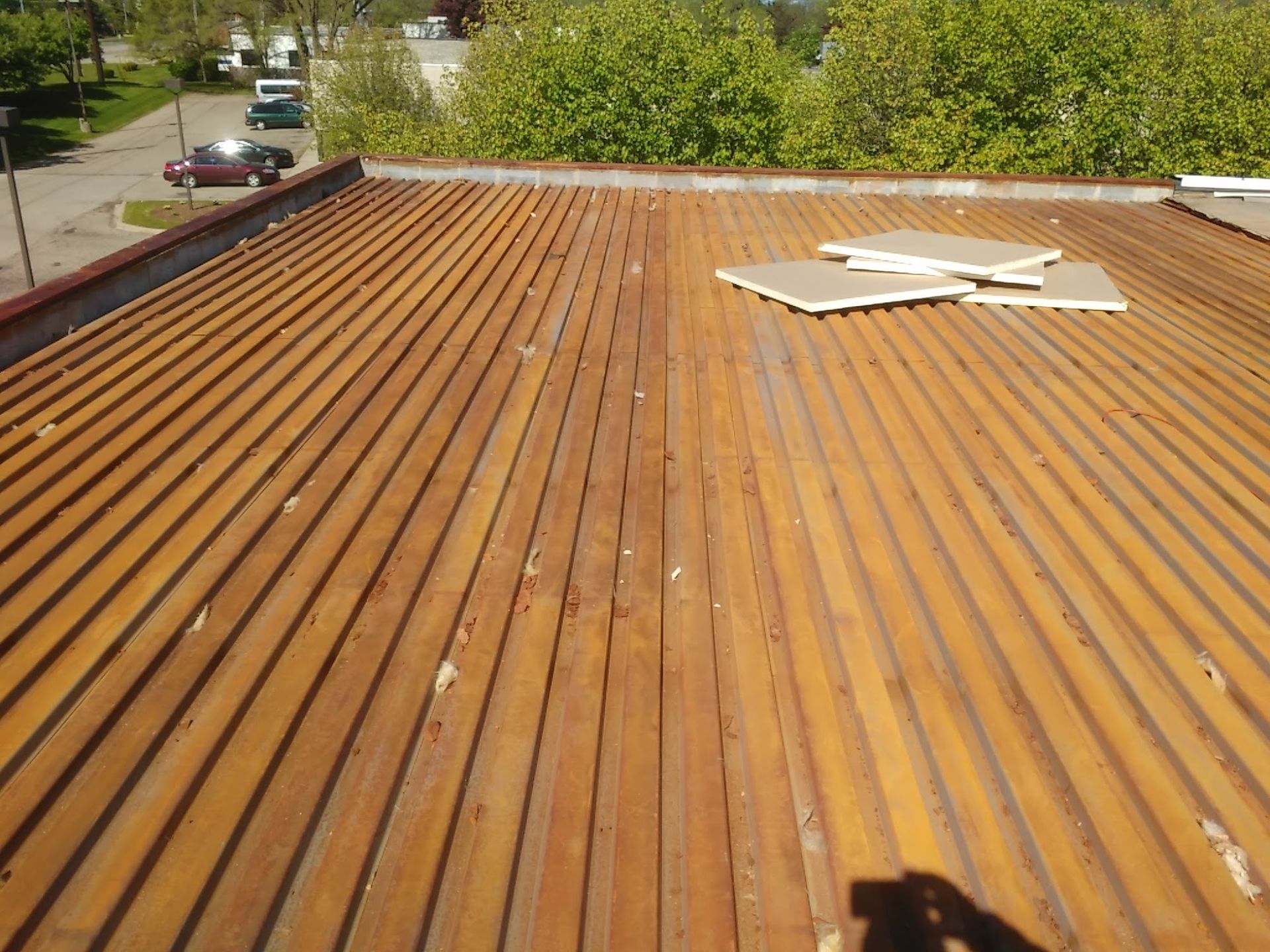 Rusty corrugated metal roof with a few boards and trees visible beyond the edge