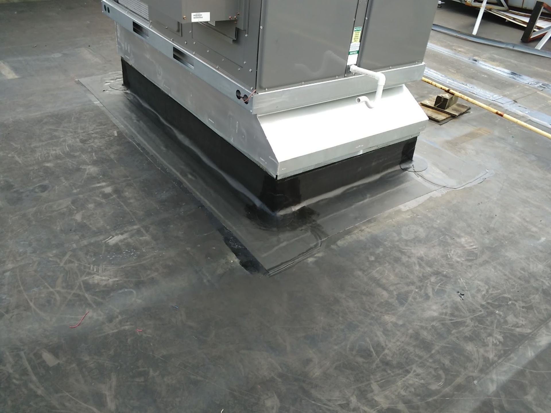 Industrial HVAC unit on a flat rooftop with black roofing membrane and a white metal base