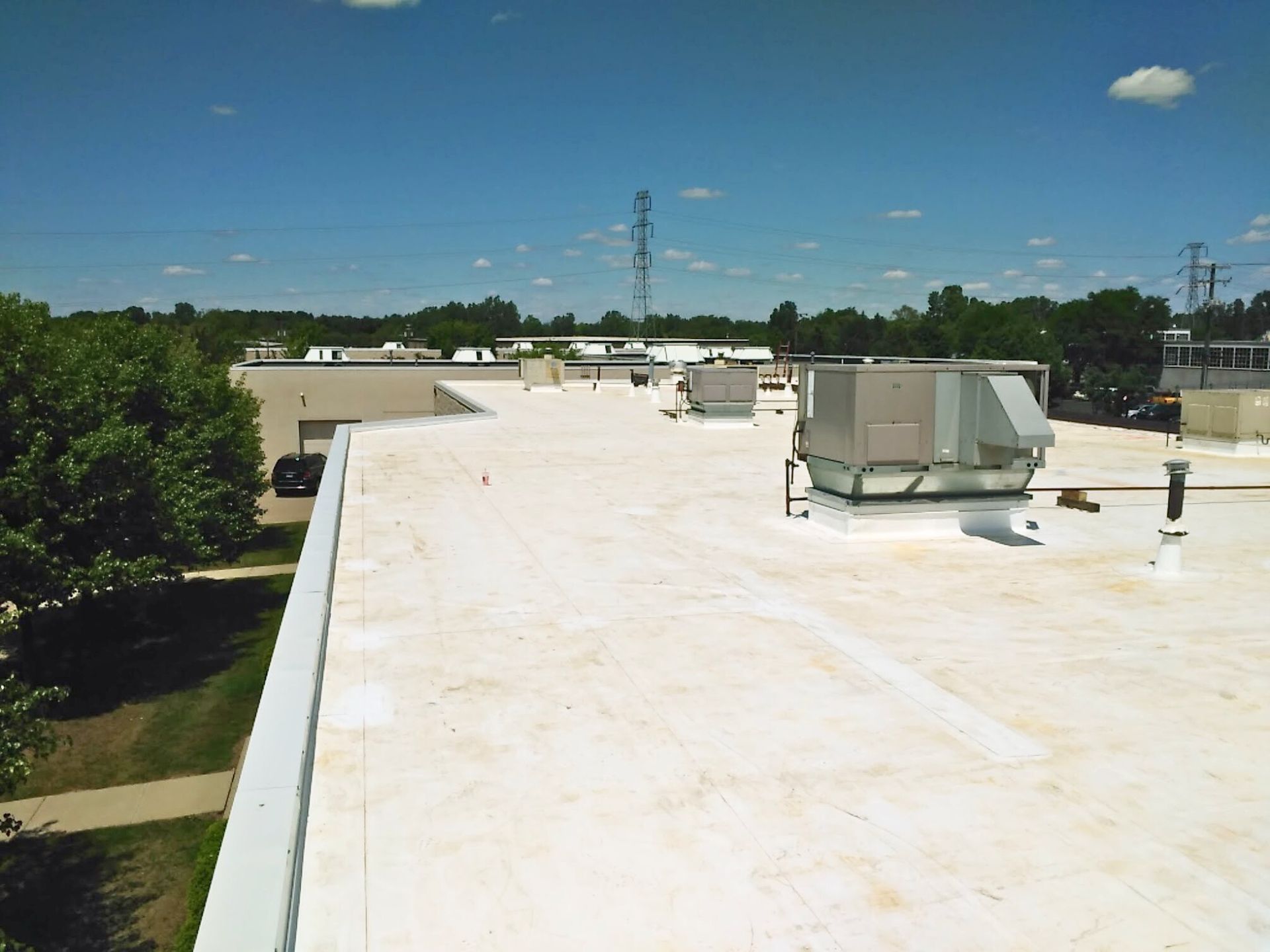Rooftop with white coating, HVAC units, and clear blue sky above surrounding trees