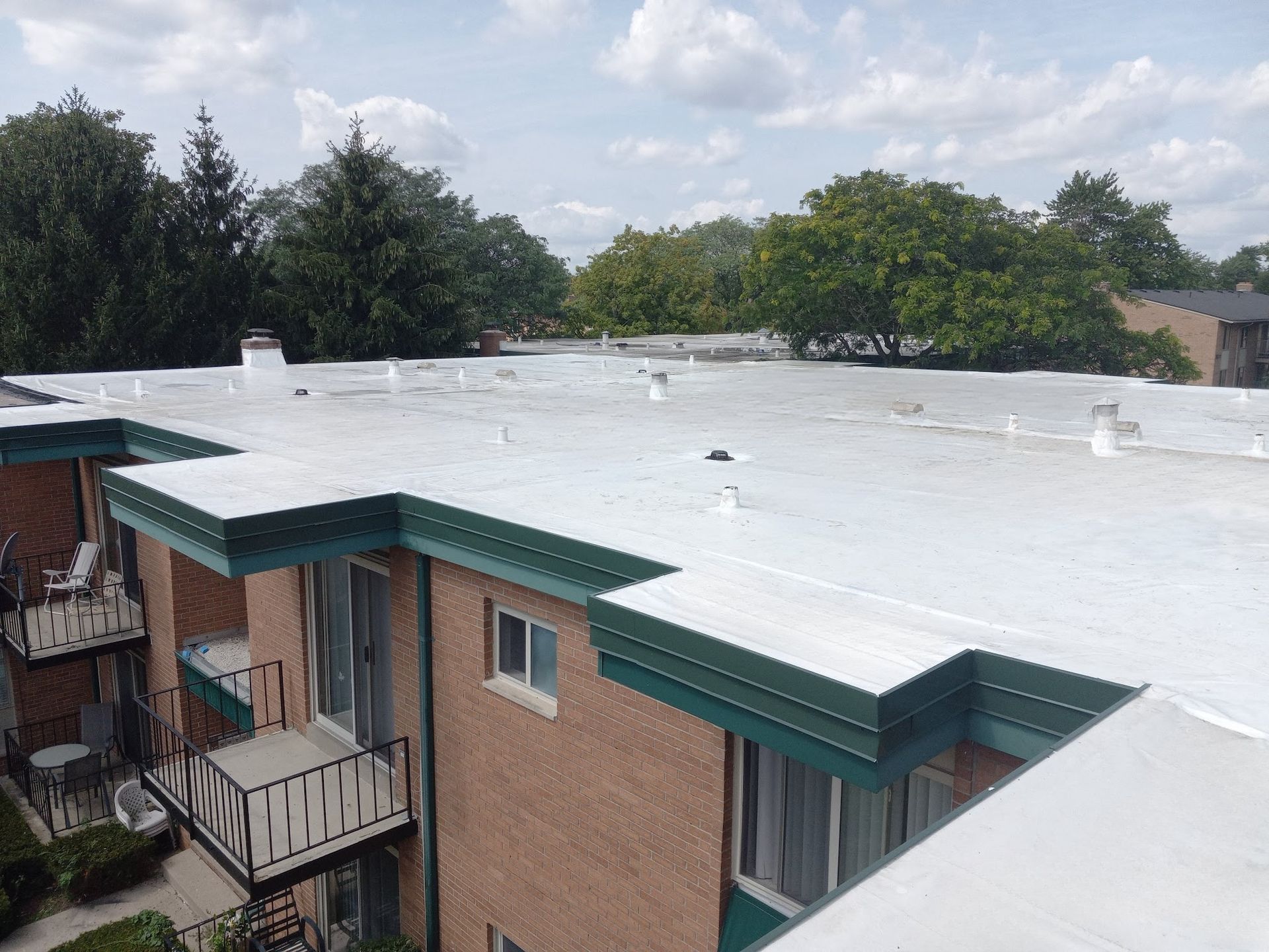 Flat rooftop with white coating on a brick apartment building, viewed from above with trees in the background