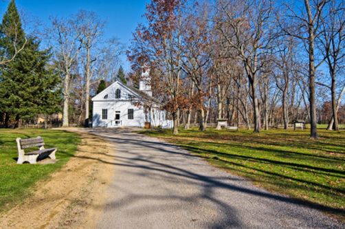 A white house is sitting on the side of a dirt road surrounded by trees.