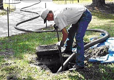 A man is digging a hole in the ground with a hose.