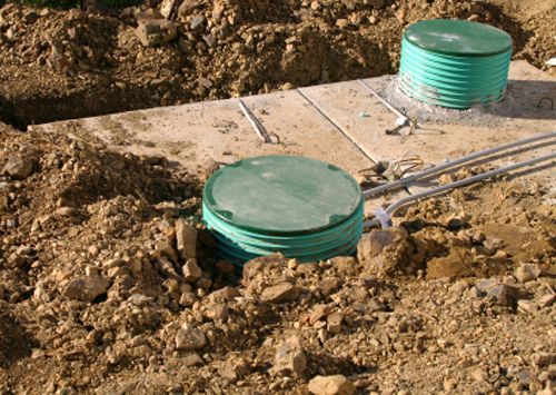 Two green barrels are sitting on top of a pile of dirt.