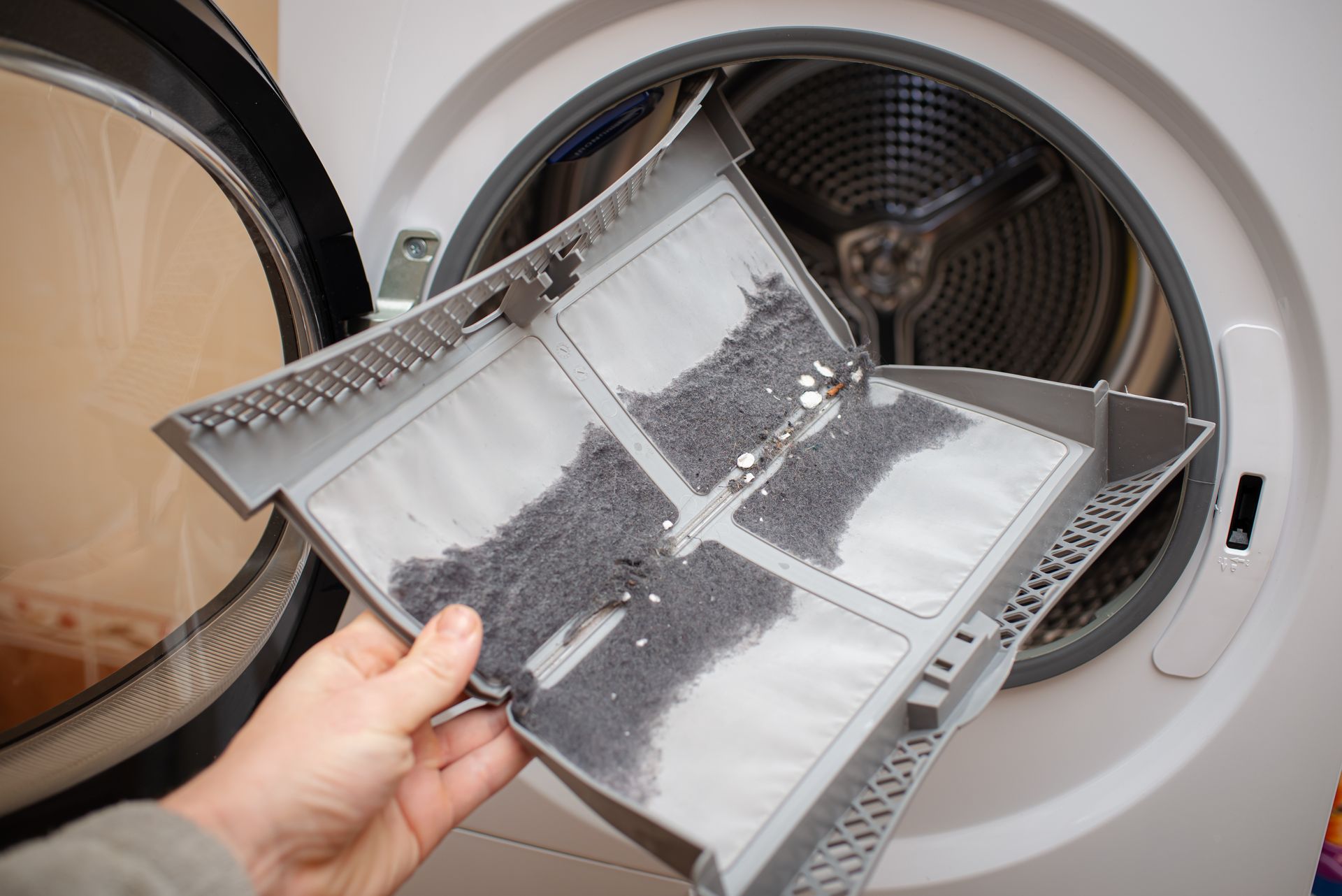 Hand holding a lint filter from an open dryer, covered with gray lint. Hand holding a lint filter from an open dryer, covered with gray lint.