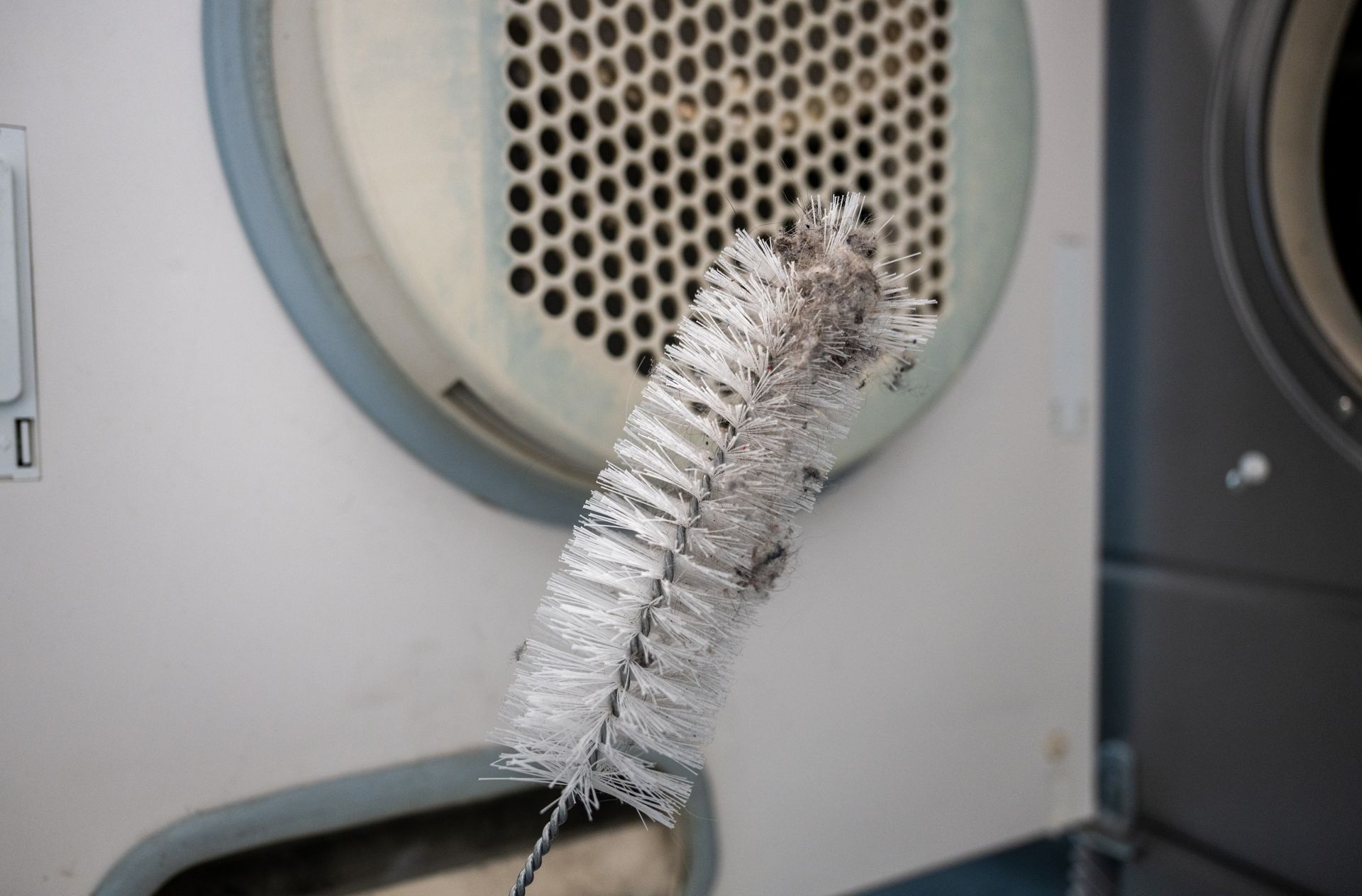 White pipe cleaner in front of a round dryer vent grille with lint buildup.