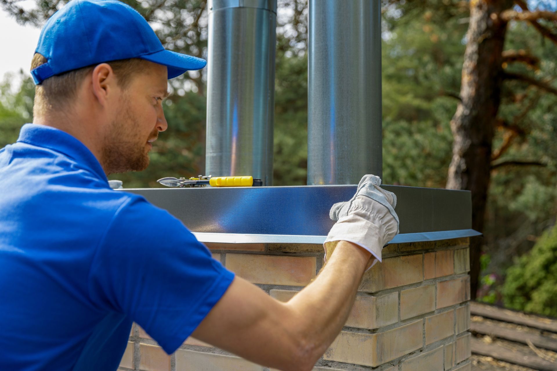 Worker in blue cap and shirt measuring a chimney with a level outdoors.