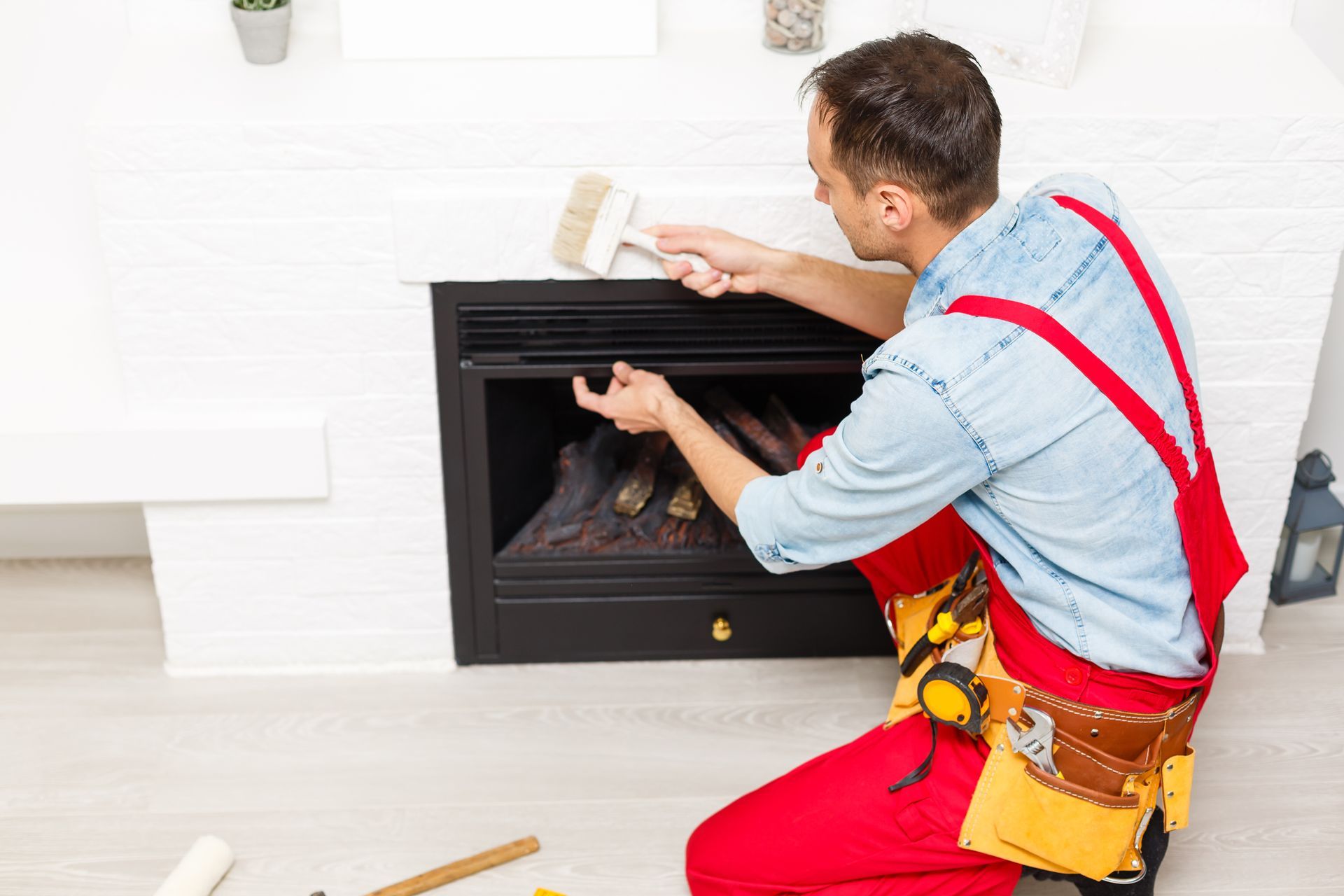 Worker installing a black fireplace insert with a brush and tools in a white room.