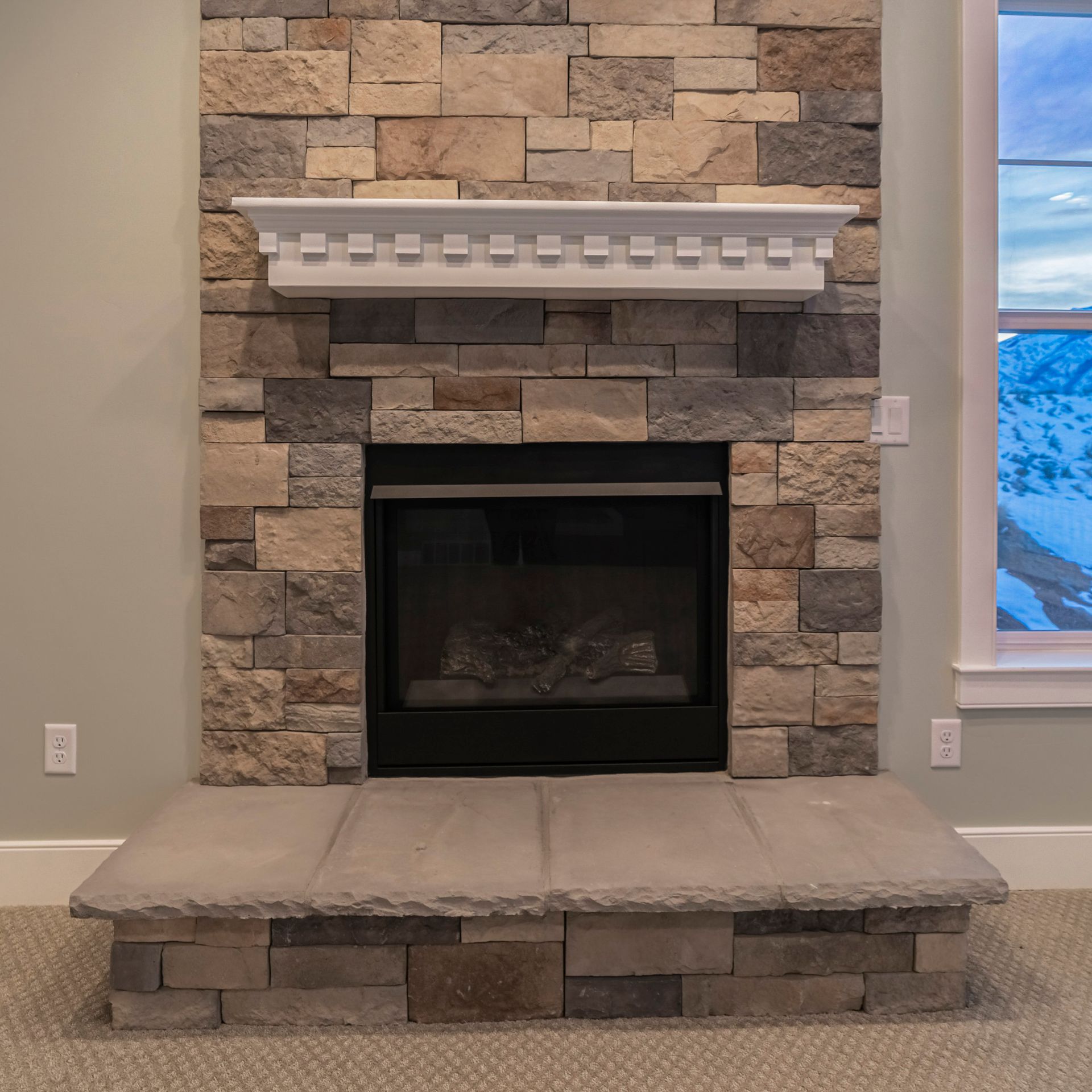 Stone fireplace with white mantel and hearth in a living room, with a window on the right.