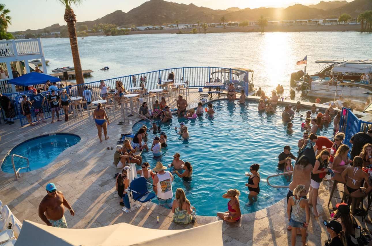 A large group of people are gathered around a large swimming pool.