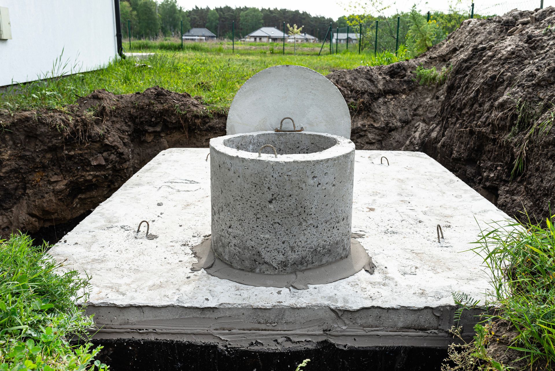 Concrete septic tank, partially buried in a yard, with lid and access hole open.