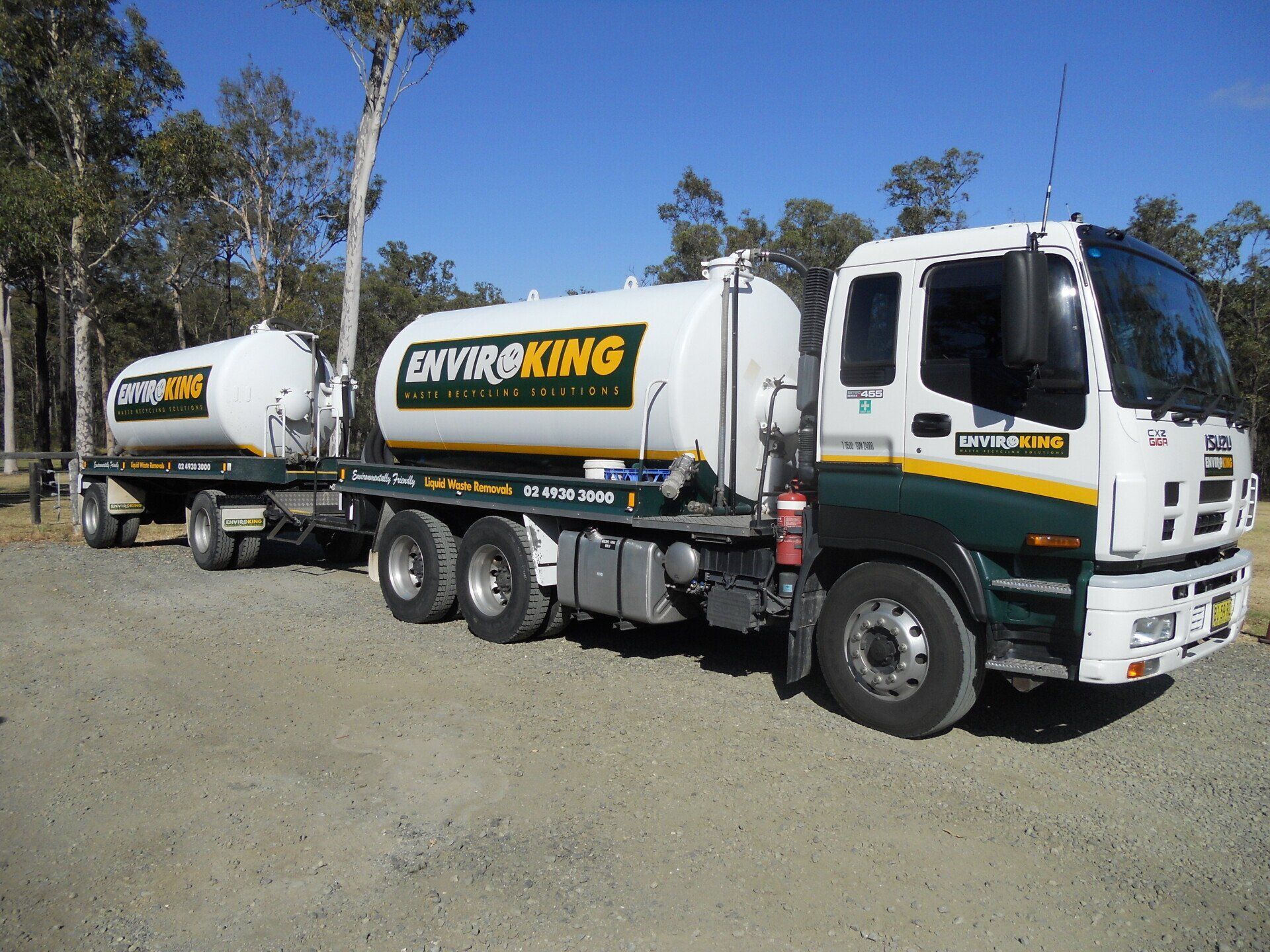 White Enviro King tanker truck and trailer parked on gravel road with trees in the background.